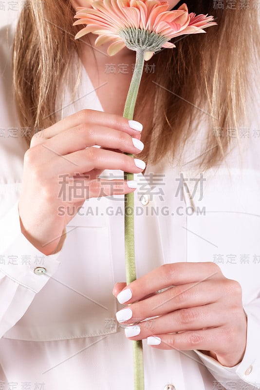 裁剪图像的女孩在牛仔裤和t恤拿着一朵红色的花在她的手与美甲在一个白色的背景