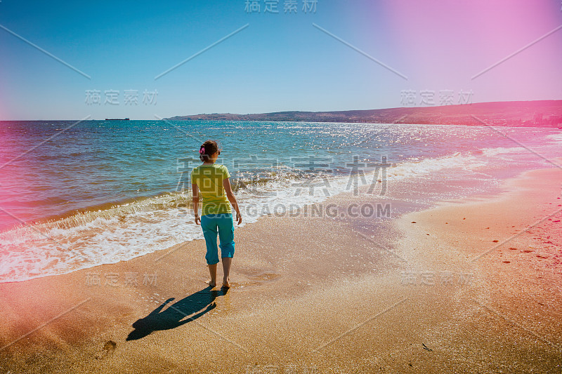 年轻快乐的女人光着脚走在海滩上，夕阳西下