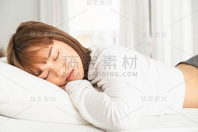枕在床上睡觉的女人，头靠在枕头上，手放在头旁边。被子一直盖到她的肩膀，舒适而幸福。拂晓的阳光照在她脸