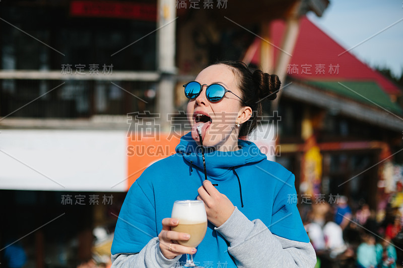 年轻女子滑雪戴着太阳镜喝咖啡从玻璃帽户外在冬季滑雪胜地