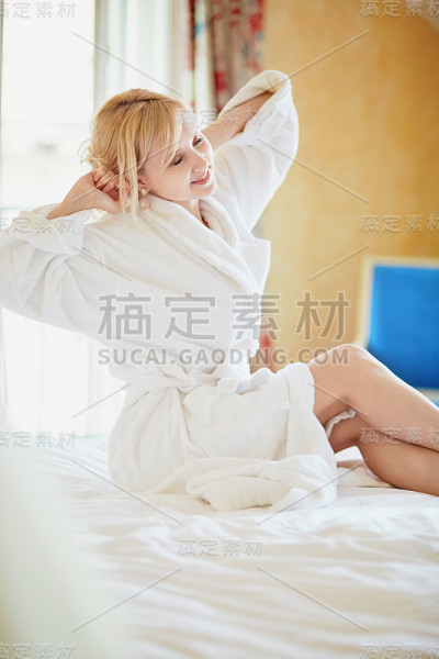 穿着白色浴袍的漂亮年轻女子坐在床上