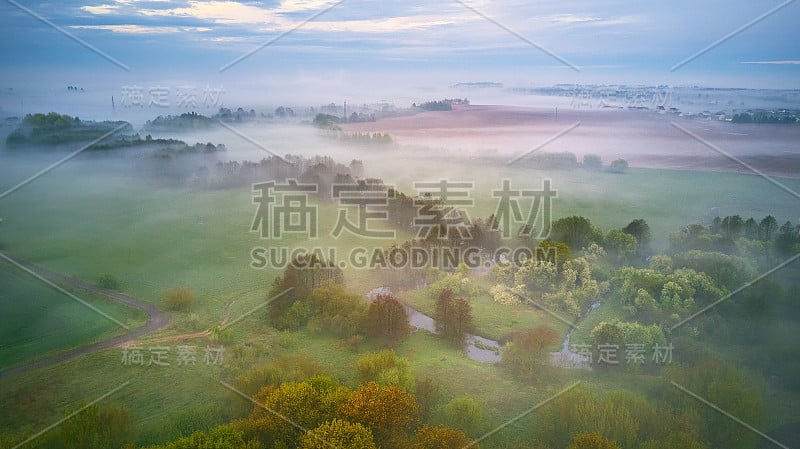 夏季多云多雨多雾的早晨全景图。农村雾蒙蒙的河流、田野、草地、村庄。春天天气阴沉沉的。盛开的树木