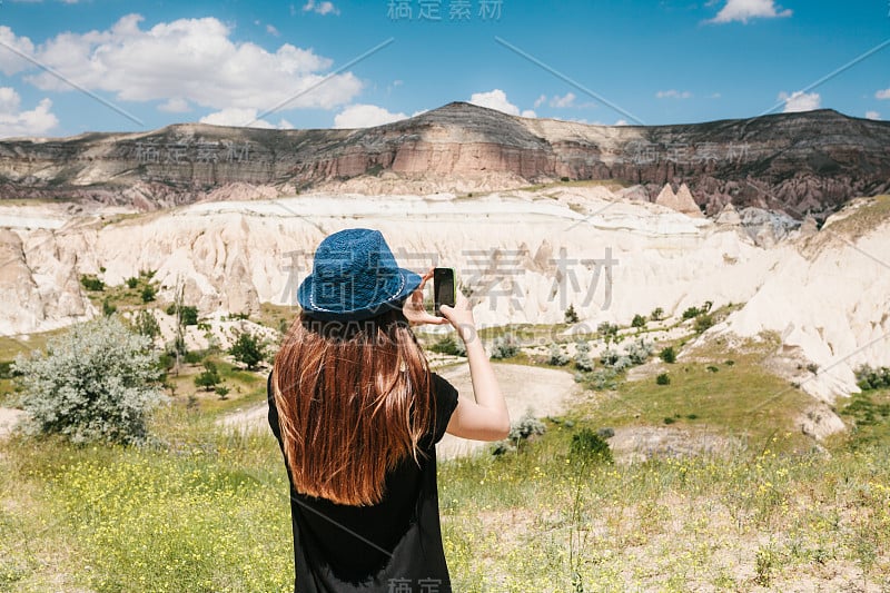 一名女游客在手机上拍摄了一张照片，以纪念土耳其卡帕多西亚美丽的山景。旅游，旅游，远足，度假。