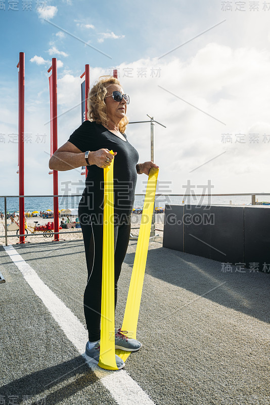 成熟女性(70-75岁)在巴西里约热内卢伊帕内玛海滩的露天健身房用弹力绳锻炼