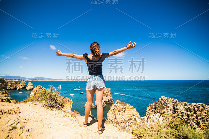 美丽的拉丁女人站在海上的岩石上迎接夏天的到来