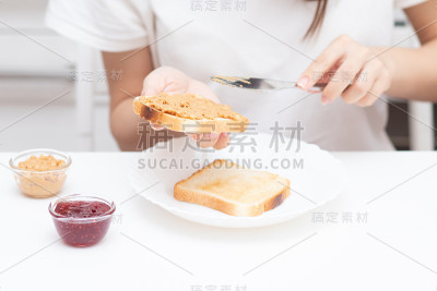 女性用手把花生酱糊涂在面包上，早上在家为全家准备三明治当早餐