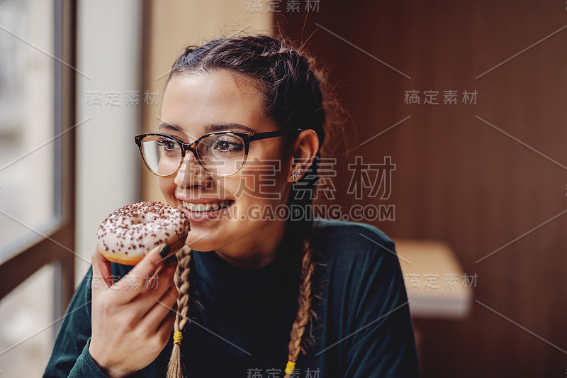 肖像微笑少女坐在糕点店，拿着甜甜圈，享受自由时间。