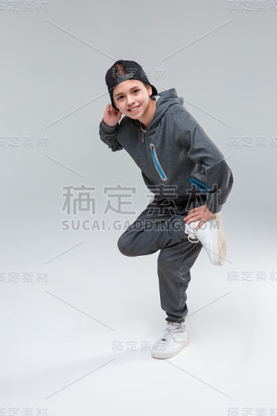 一个快乐的小男孩用另一条腿站着。在一个灰色的背景。