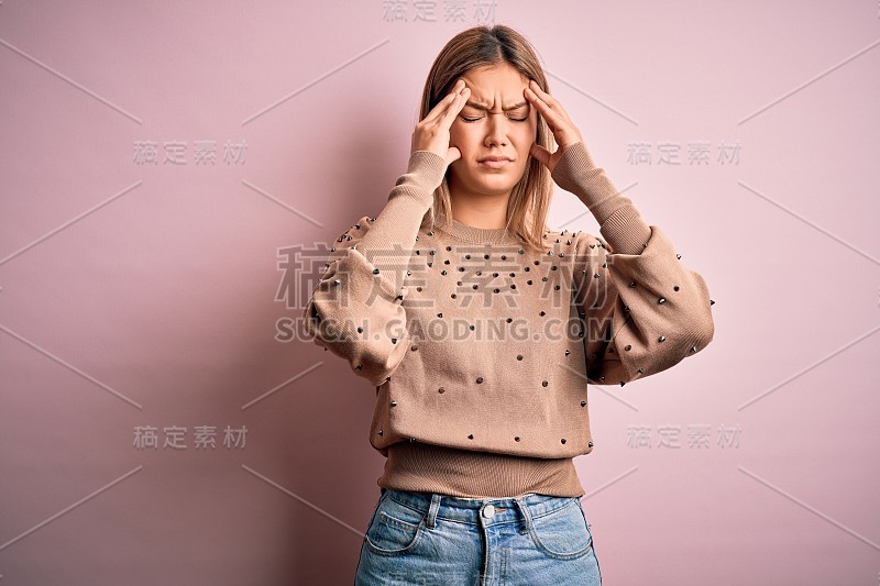 年轻美丽的金发女人穿着时尚的毛衣在粉红色孤立的背景下遭受头痛绝望和压力，因为疼痛和偏头痛。手放在头上