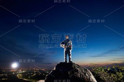 太空旅行者站在夜空下的岩石山上。