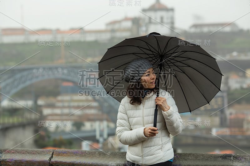 葡萄牙波尔图，多云的天气里，一名亚洲女游客撑着雨伞，拍摄于多姆·路易斯一世大桥。