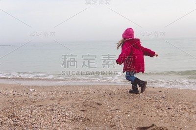 穿着红夹克的小女孩在海滩上玩海浪