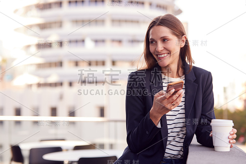 女商人站在办公大楼外用手机，背景是城市天际线