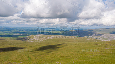 在暴风雨的白云天空下，一个山谷与绿色的斜坡和乡村的背景鸟瞰图