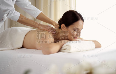 漂亮的黑发女子享受水疗沙龙的背部按摩程序。美丽的概念
