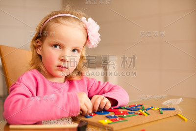 可爱的小女孩用针尖把积木钉在木板上玩玩具