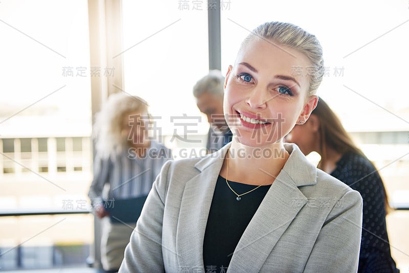 年轻的女商人面带微笑，同事们在后面交谈