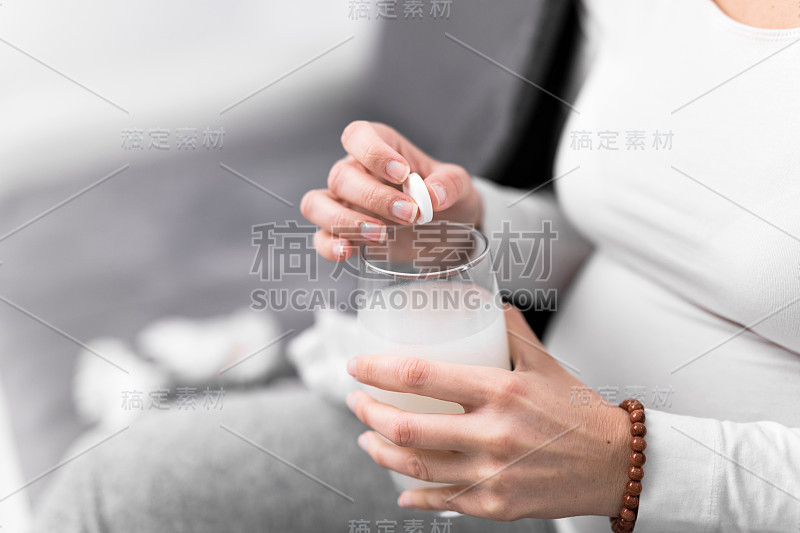 孕妇在一杯水中服用维生素片。