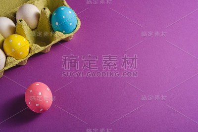 彩色的圆点复活节彩蛋在蛋盘上紫色紫罗兰素色的背景，贺卡，拷贝空间，角度视图