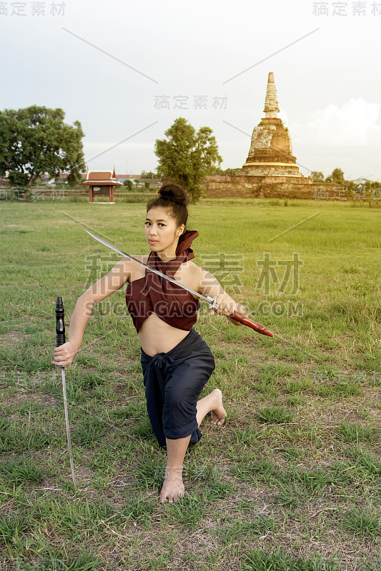 漂亮的亚洲女人在泰国古代武士摆姿势，并在她的手握双剑。