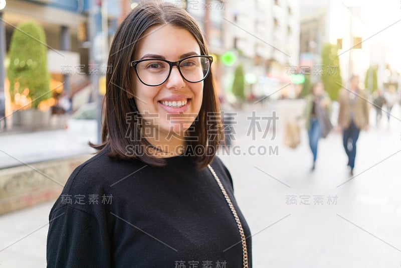 美丽年轻的黑发女人微笑着兴奋地走在城市的街道上，快乐和自信的表情站在城镇的户外