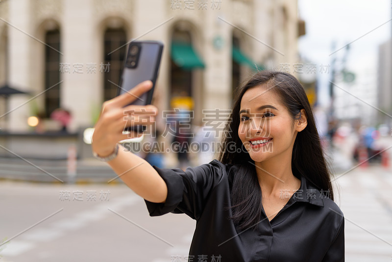 亚洲女商人在城市的户外街道上用手机做视频博客或自拍