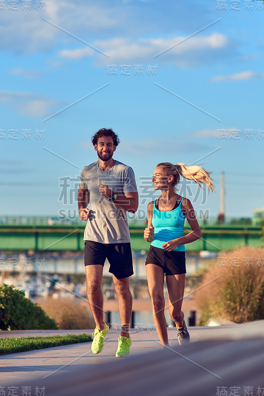 现代女人和男人在河边的城市环境中慢跑/锻炼。