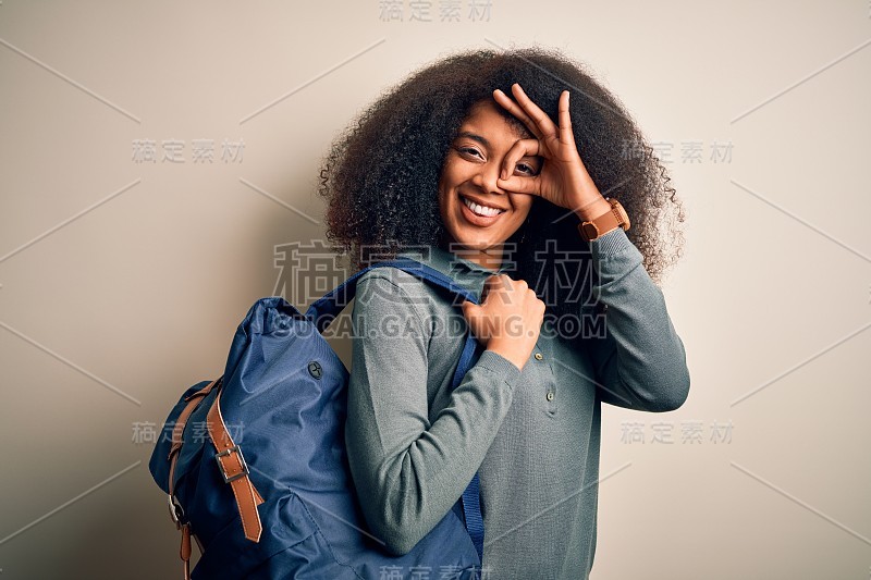 年轻的非洲裔美国学生女人与非洲发式戴背包在背景与快乐的脸微笑做ok手势与手在眼睛透过手指看