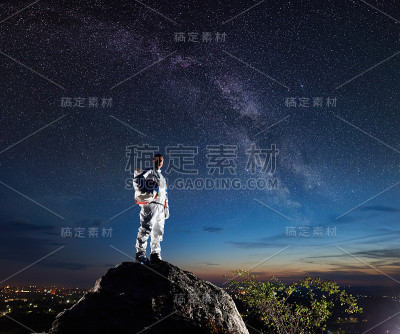 宇航员站在岩石山在夜空下繁星点点。