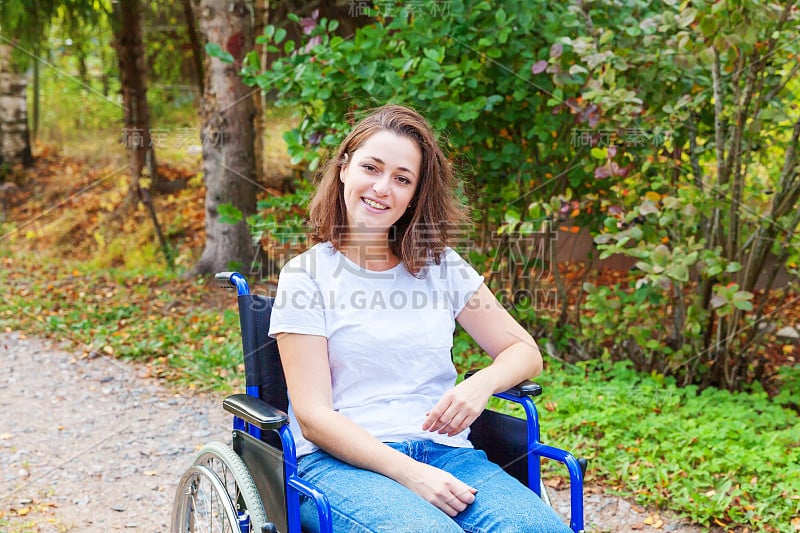 年轻快乐的残疾妇女在医院公园的道路上等待病人服务。瘫痪的女孩坐在残疾人专用轮椅上，在户外大自然中。康