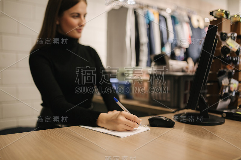 年轻的店员在服装店用电脑工作。美丽的女职工