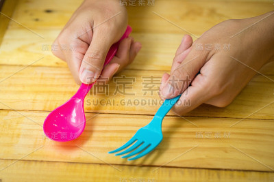 木制背景上，塑料勺子和塑料叉子在手
