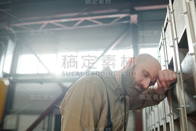 生病或疲惫的工厂工人站在金属建筑