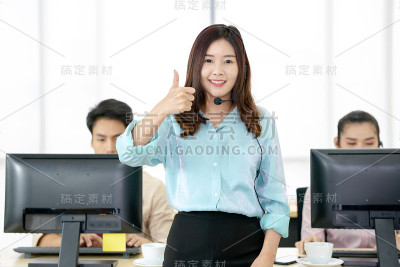 美丽的女人，作为呼叫中心的领导，而她站着，微笑着周围的同事。