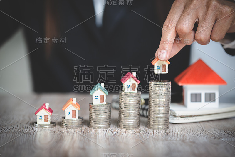 女人的手把房子模型放在硬币堆上。Concept for property ladder，规划攒钱买房