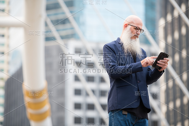 成熟的秃头商人在城市户外使用电话