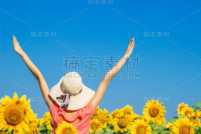 卷毛漂亮的女孩戴着帽子在黄色的向日葵的田野里玩