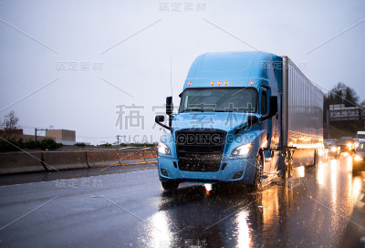 现代大卡车蓝色半挂车与拖车驾驶在雨天潮湿的高速公路与前灯反射