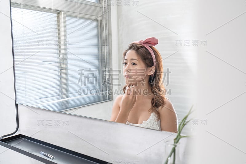 近距离的微笑女人化妆刷近脸和看镜子。亚洲美女