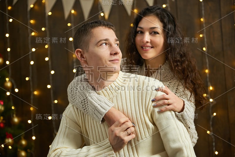 新人在圣诞彩灯和装饰，身穿白色，年轻的女孩和男人，冷杉树在黑暗的木制背景，冬季节日的概念