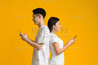 亚洲夫妇背靠背站着，用手机