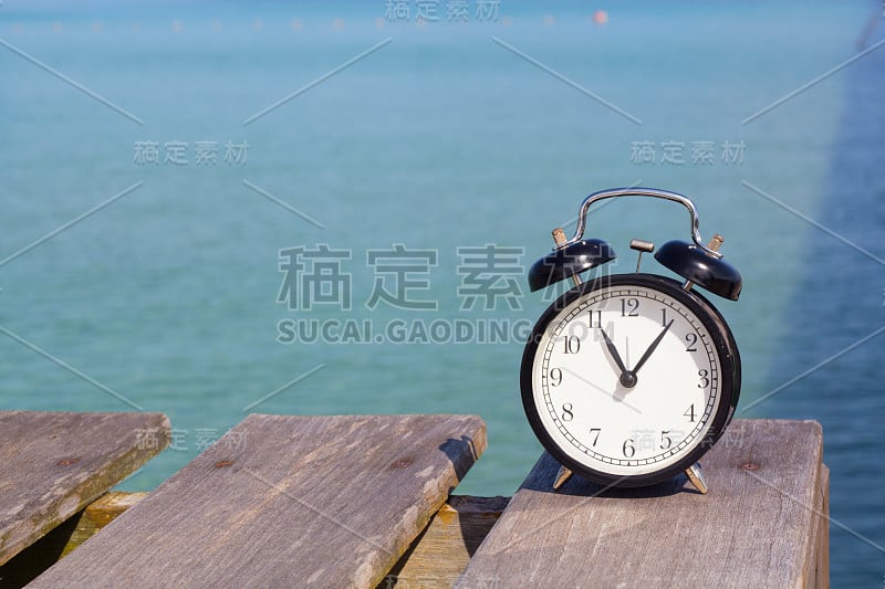 11点u2019时钟的复古闹钟放在以大海为背景的木桥上。