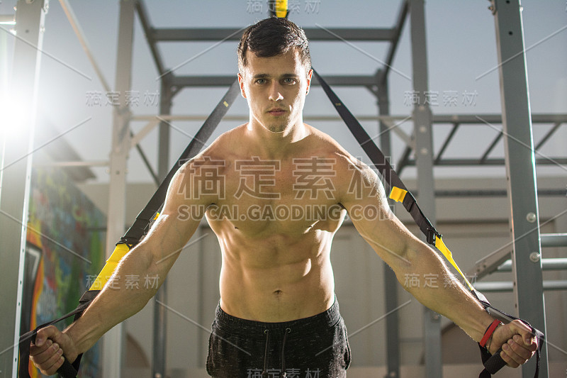 年轻英俊的赤膊男子在户外健身带锻炼。