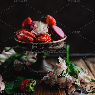 近距离的碗与马卡龙和草莓在木桌上与花