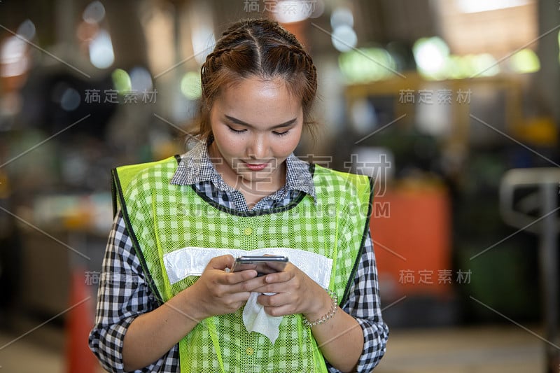 女亚洲工程师穿着制服戴着安全帽看智能手机