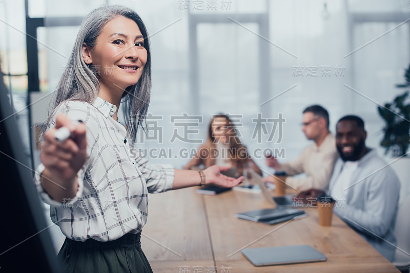 选择性地关注微笑的亚洲女商人用马克笔指着她的多元文化的同事的背景