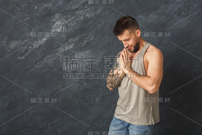 英俊的年轻人祈祷在灰色的背景