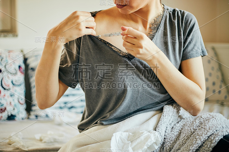 拿着体温计的妇女因发高烧感冒坐在床上。