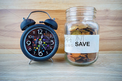 瓶内装有金币的SAVE标签，黑色闹钟和木头背景