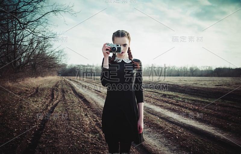 迷人的年轻女孩穿着黑色的衣服，用经典的电影相机拍照。野外写真